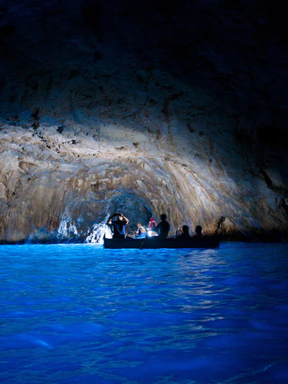 Boat tour inside Grotta Azzurra, Capri, with illuminated blue water and rocky cave walls.