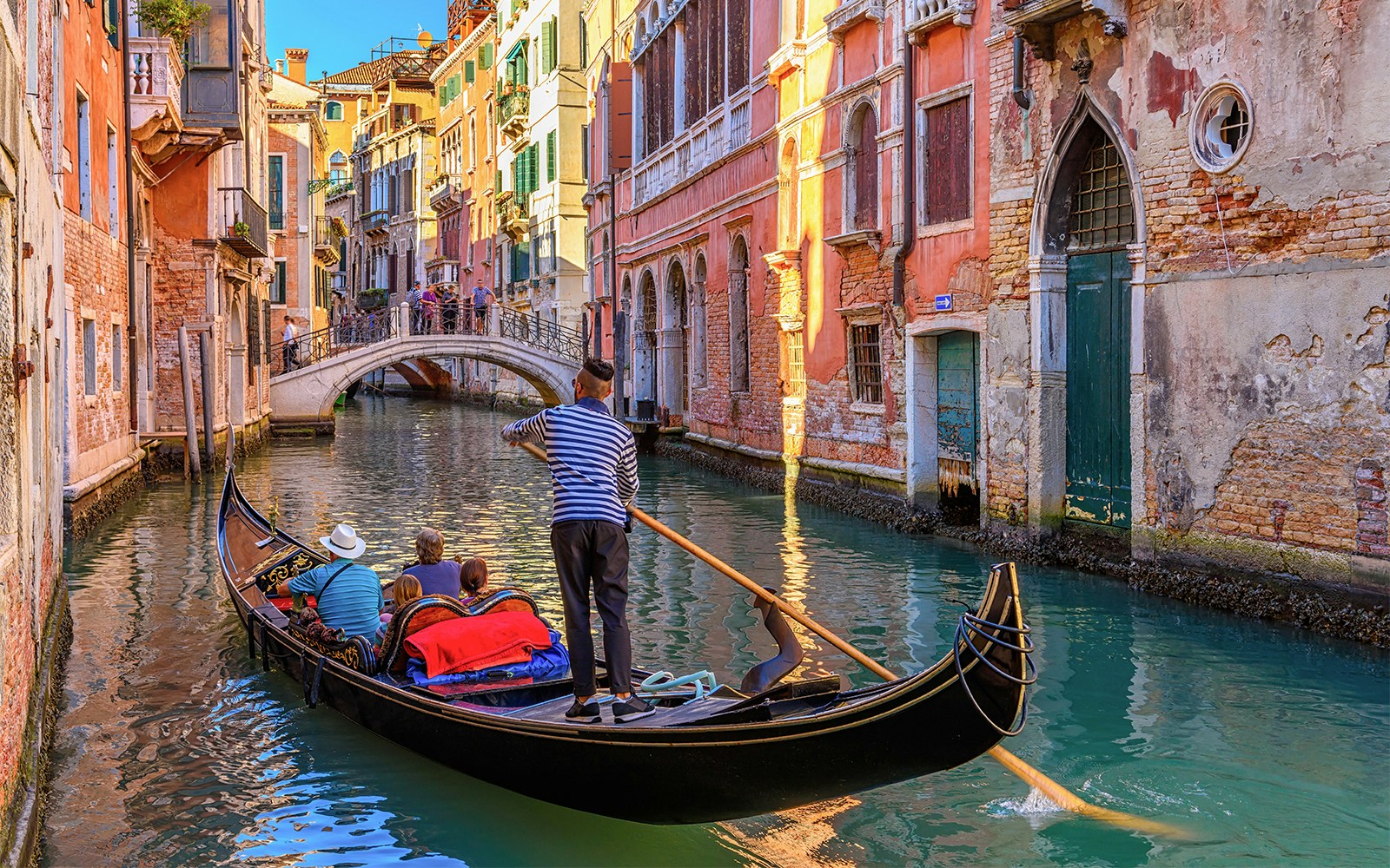 Gondola navigating a narrow canal in Venice with colorful buildings and a small bridge.