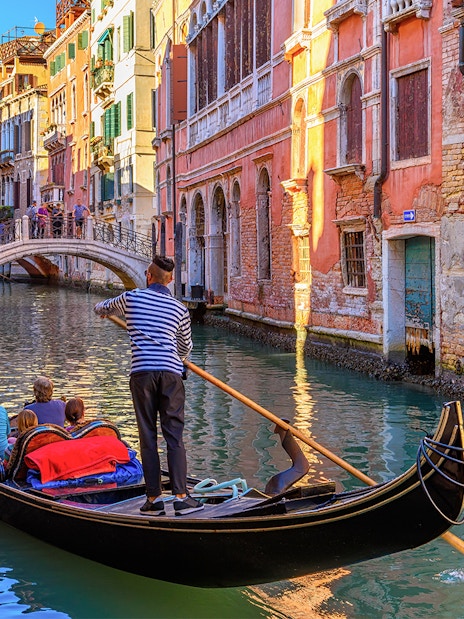 Gondola navigating a narrow canal in Venice with colorful buildings and a small bridge.