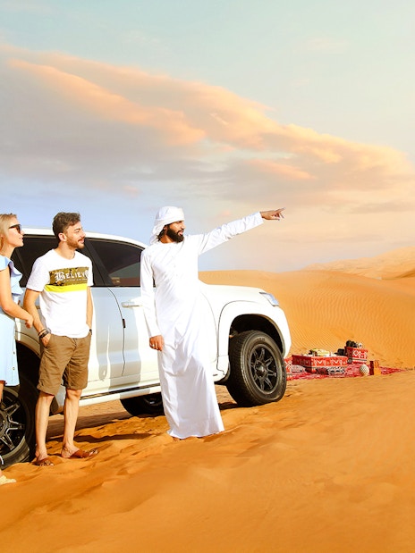 Traveller with guide beside SUV after dune bashing in desert safari.