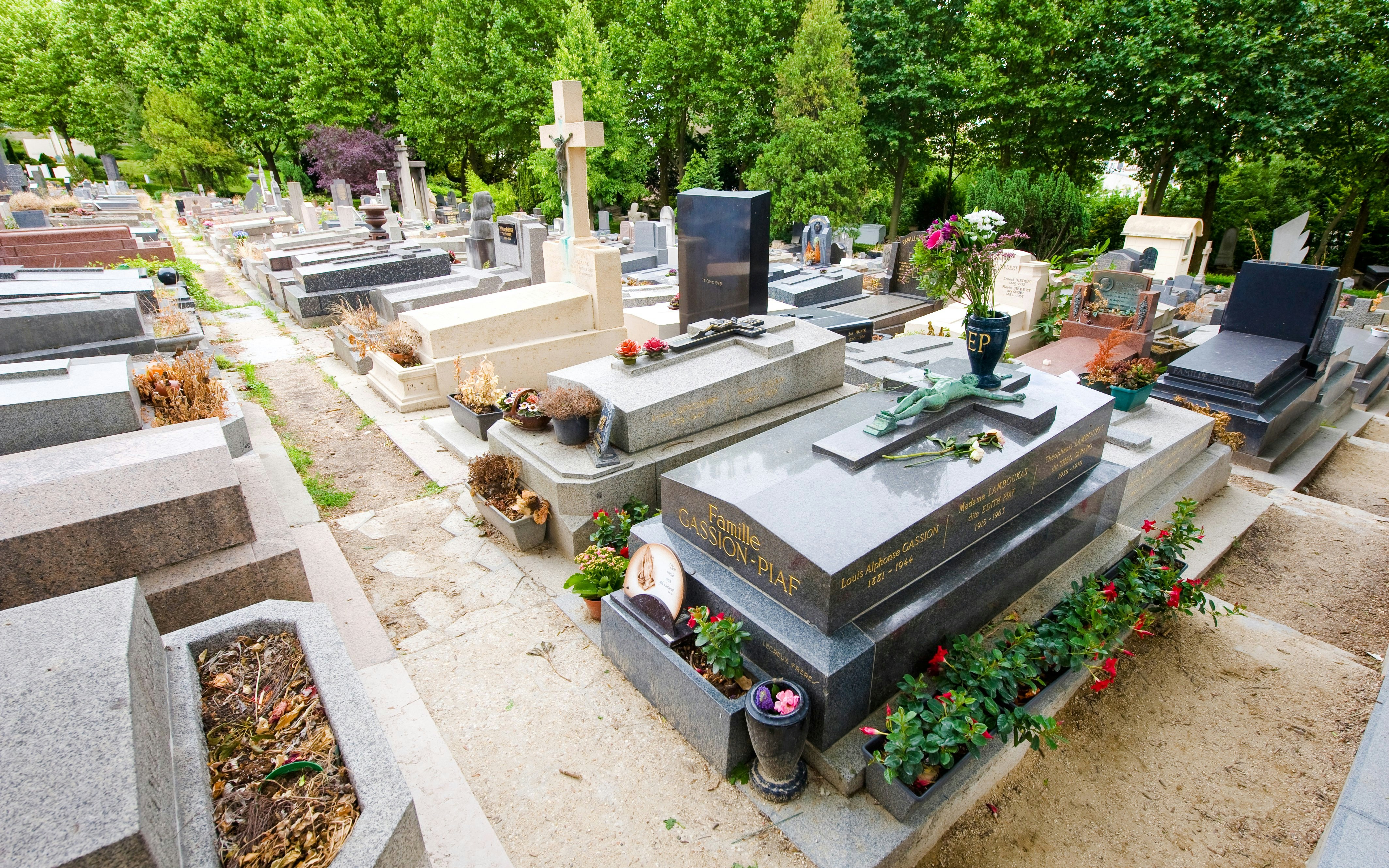 Gravesite of Édith Piaf at Père Lachaise Cemetery, Paris, surrounded by greenery and flowers.
