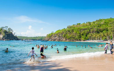 Tourists swimming at Crystal Bay Beach, West Nusa Penida Island, with lush hills in the background.