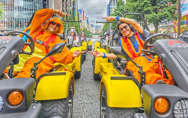 Participants in costumes driving go-karts on the Uptown Go Kart Tour in a city street.