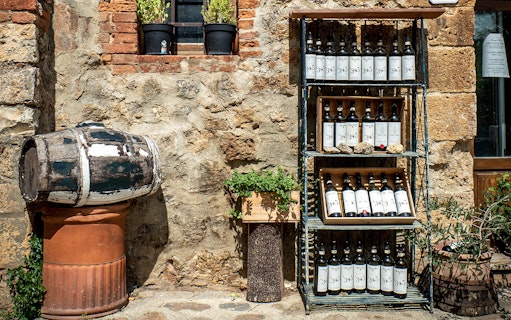 Wine bottles on a shelf and a rustic barrel in Chianti courtyard during e-bike tour.