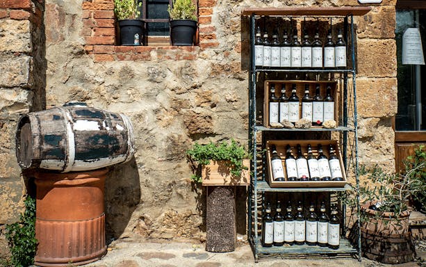 Wine bottles on a shelf and a rustic barrel in Chianti courtyard during e-bike tour.
