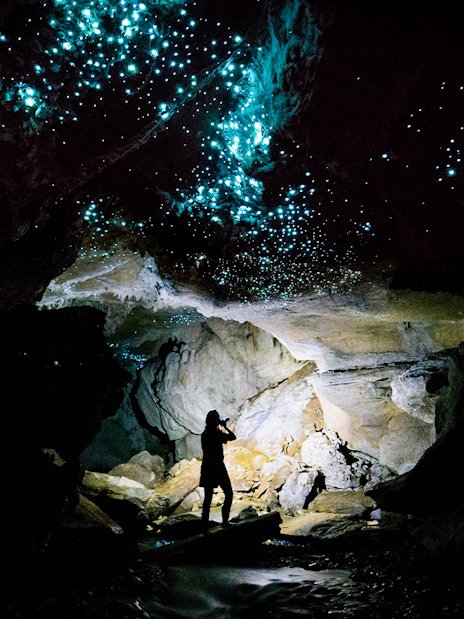 Glowworms illuminating Waitomo Caves with a silhouetted person on a guided tour.