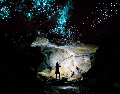 Glowworms illuminating Waitomo Caves with a silhouetted person on a guided tour.