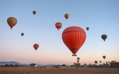Hot air balloons floating over a desert landscape at sunrise.