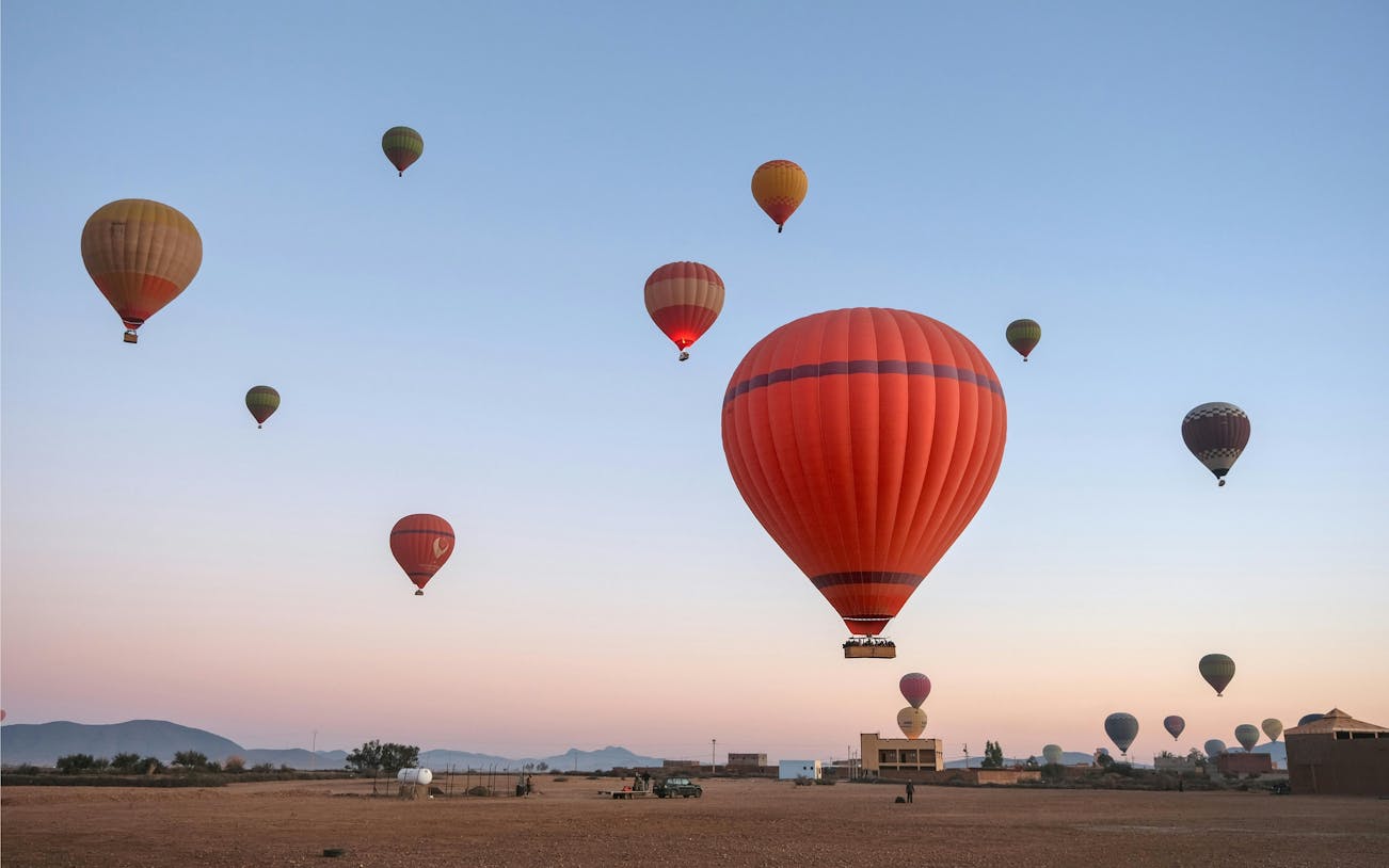 Hot air balloons floating over a desert landscape at sunrise.