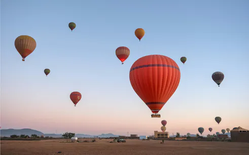 Hot air balloons floating over a desert landscape at sunrise.
