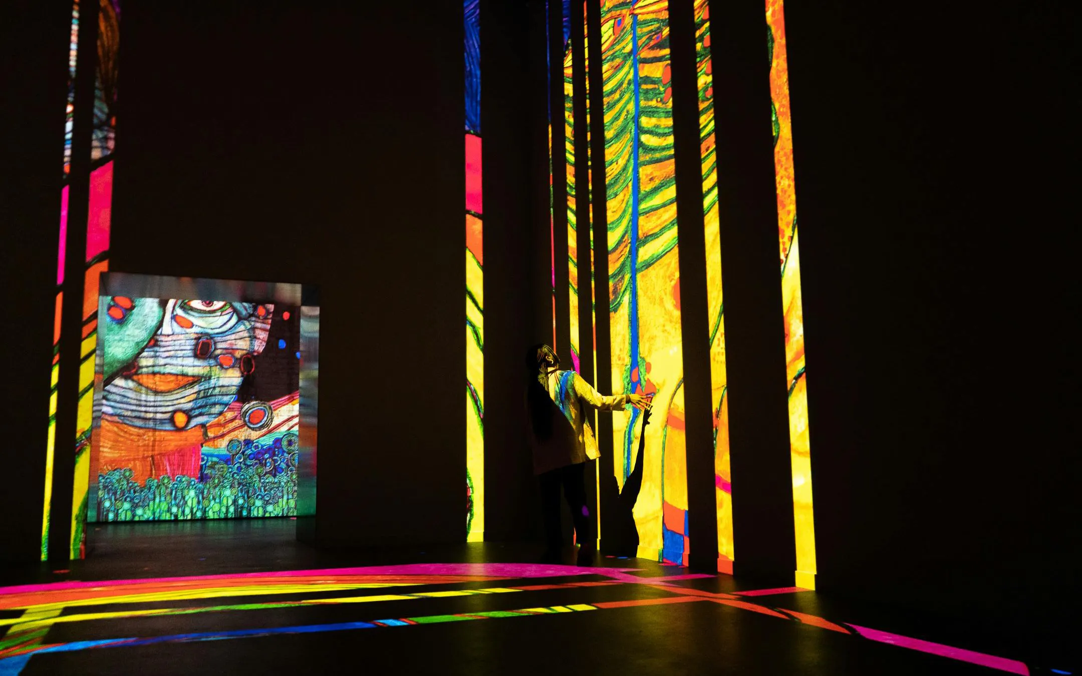 Person interacting with vibrant digital art projections at Fabrique des Lumières.