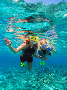 Mother and child snorkeling with masks in clear tropical waters.