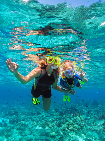 Mother and child snorkeling with masks in clear tropical waters.