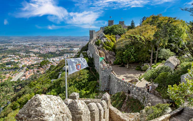 Ancient Moorish Castle walls overlooking Sintra city, Portugal, with lush greenery and flags.