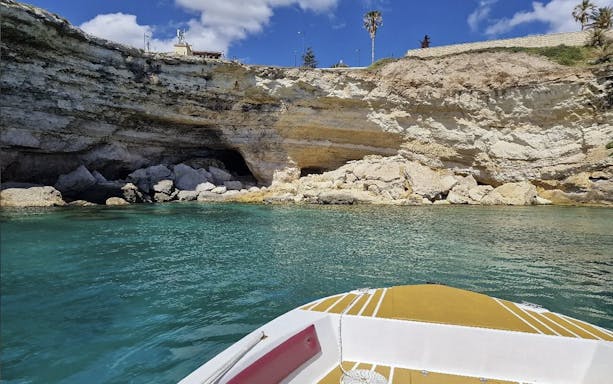 Boat approaching grotto at Ortigia Island, Sicily, with rocky cliffs and clear water.