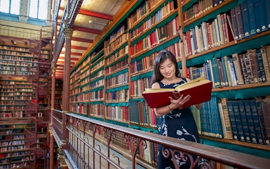 Person reading a large book in Cuypers Library at Rijksmuseum, surrounded by shelves of books.