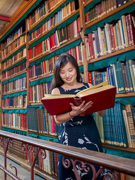 Person reading a large book in Cuypers Library at Rijksmuseum, surrounded by shelves of books.