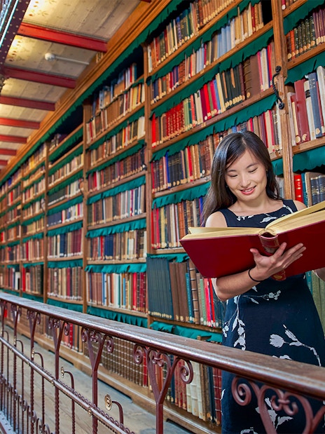 Person reading a large book in Cuypers Library at Rijksmuseum, surrounded by shelves of books.