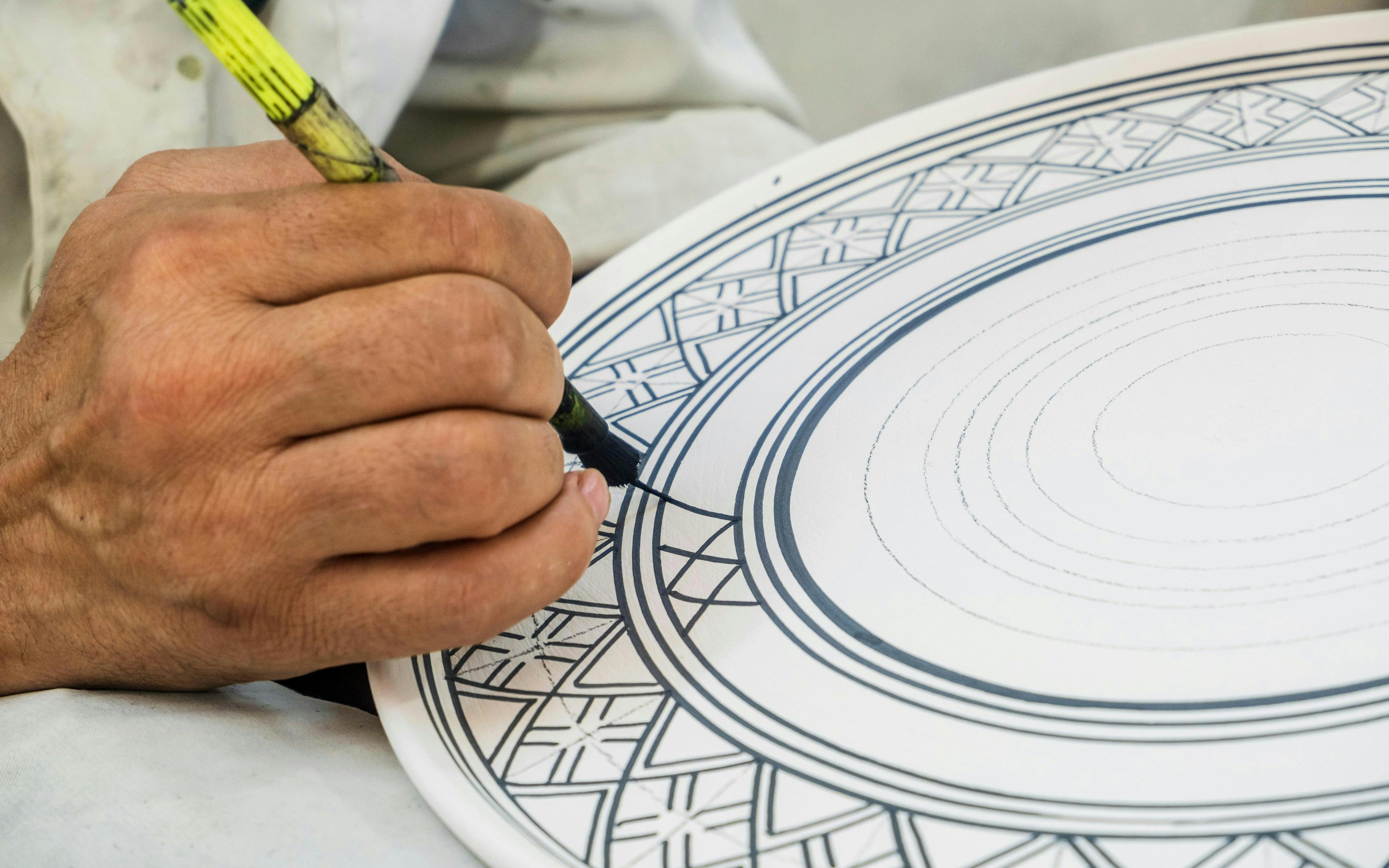 Craftsman painting intricate designs on ceramic plate in Fez pottery factory, Morocco.
