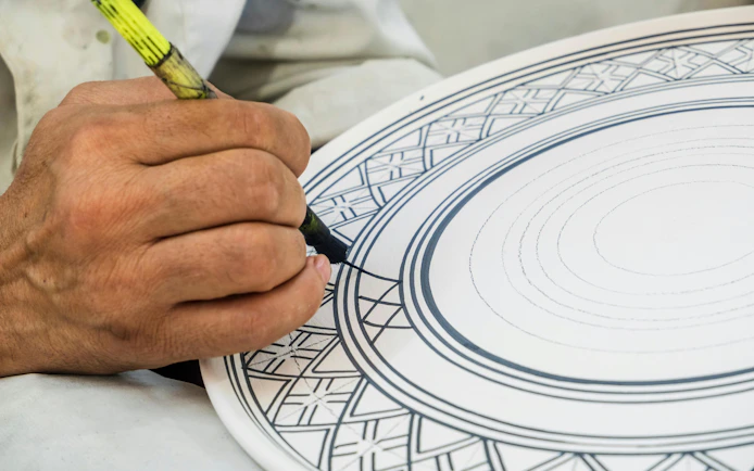 Craftsman painting intricate designs on ceramic plate in Fez pottery factory, Morocco.