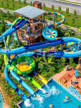 Water slides and pools at SplashMania water park with people enjoying rides.
