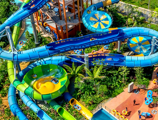 Water slides and pools at SplashMania water park with people enjoying rides.