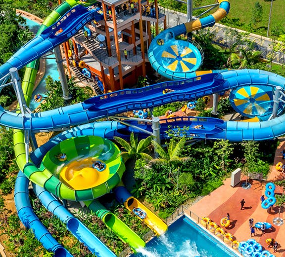 Water slides and pools at SplashMania water park with people enjoying rides.