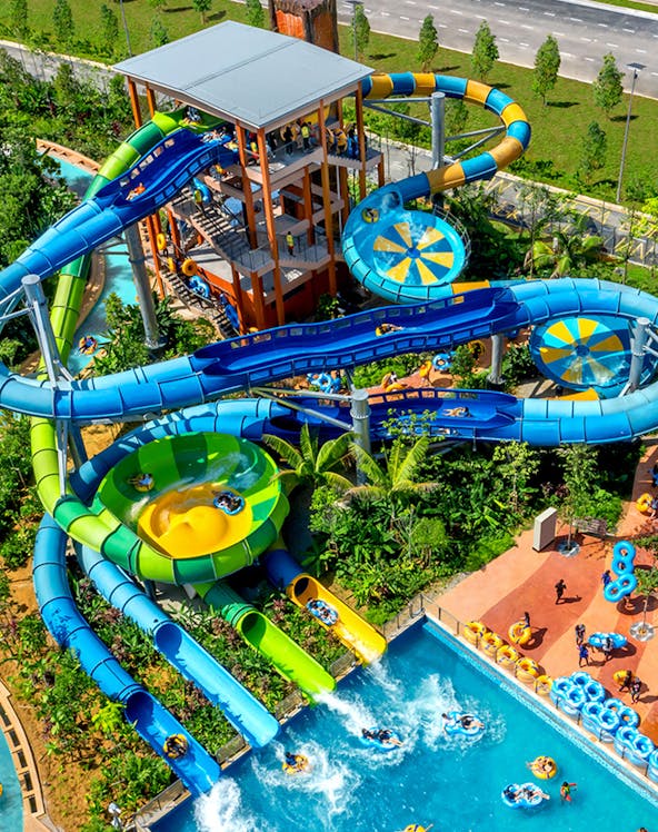 Water slides and pools at SplashMania water park with people enjoying rides.