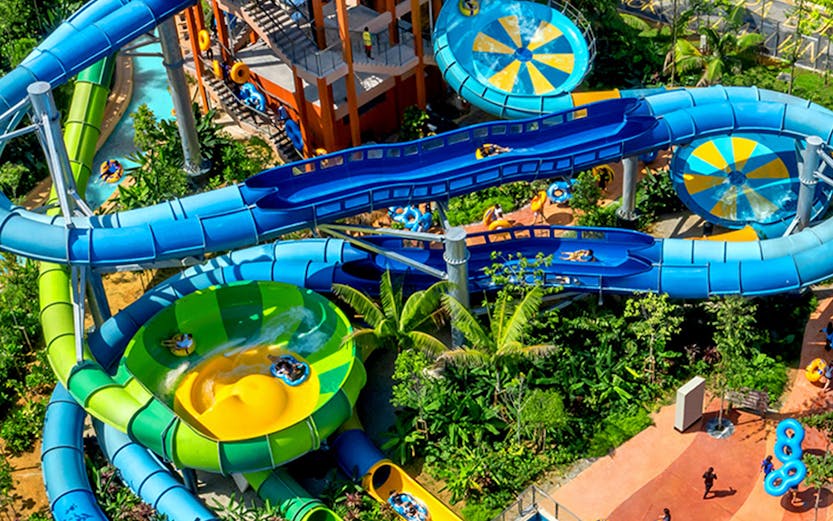 Water slides and pools at SplashMania water park with people enjoying rides.