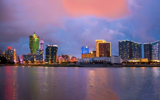 Macau skyline at dusk with neon-lit buildings reflecting on the water.
