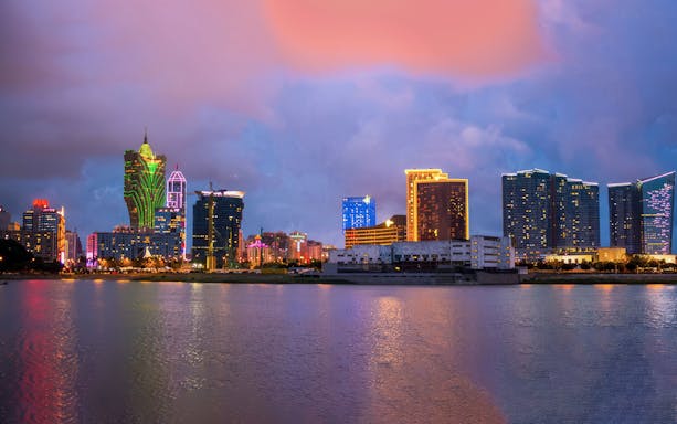 Macau skyline at dusk with neon-lit buildings reflecting on the water.