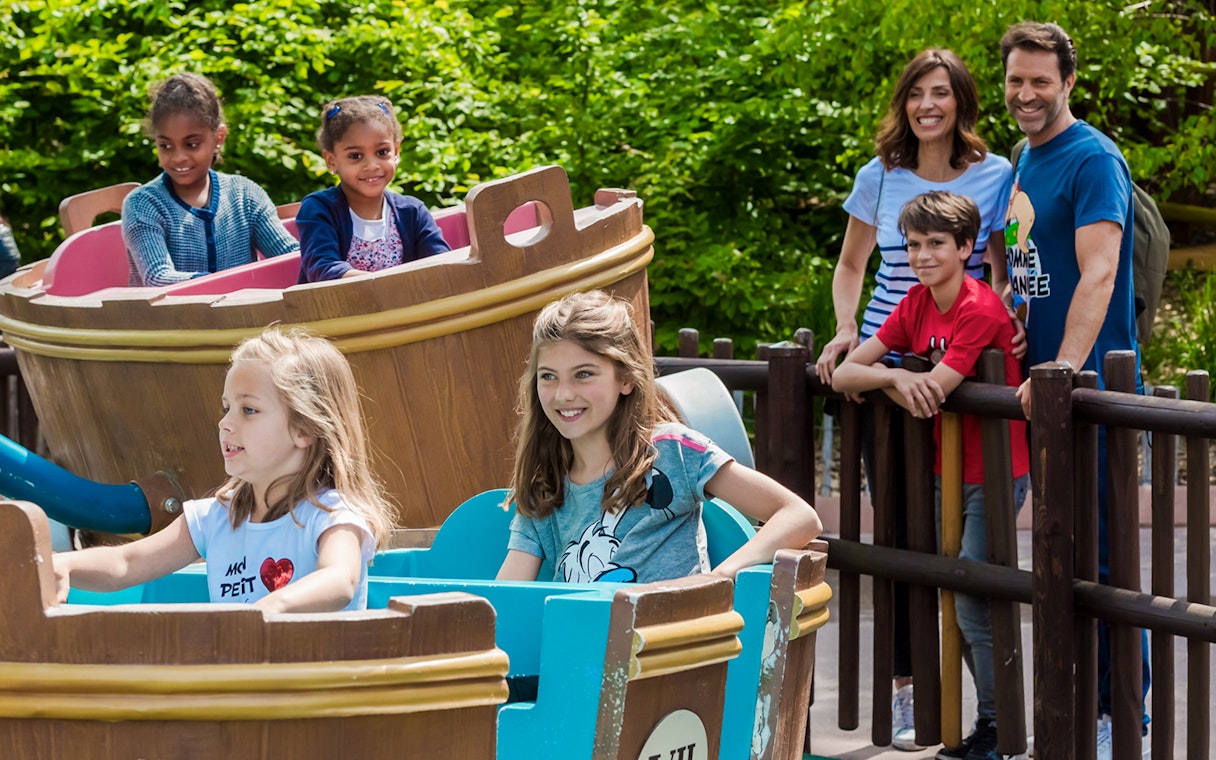 Children enjoying a boat ride at Astérix Park with family watching nearby.