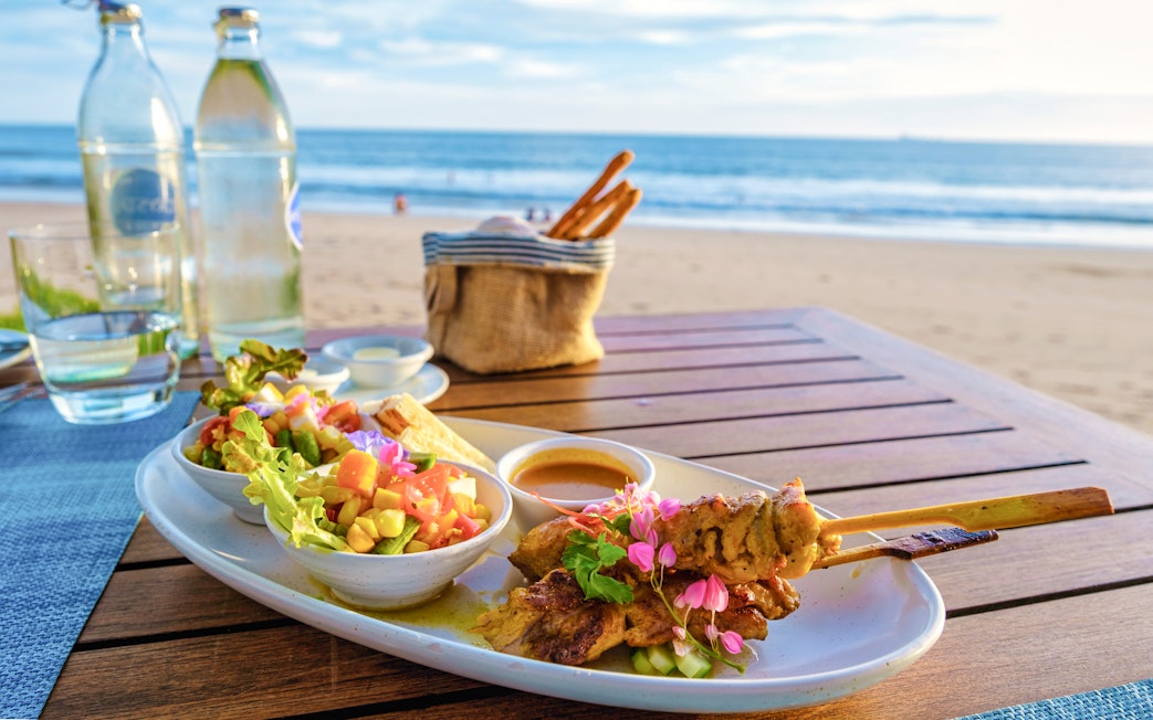 Grilled skewers and salad on a table by the beach at Nemo Island seaside restaurant.