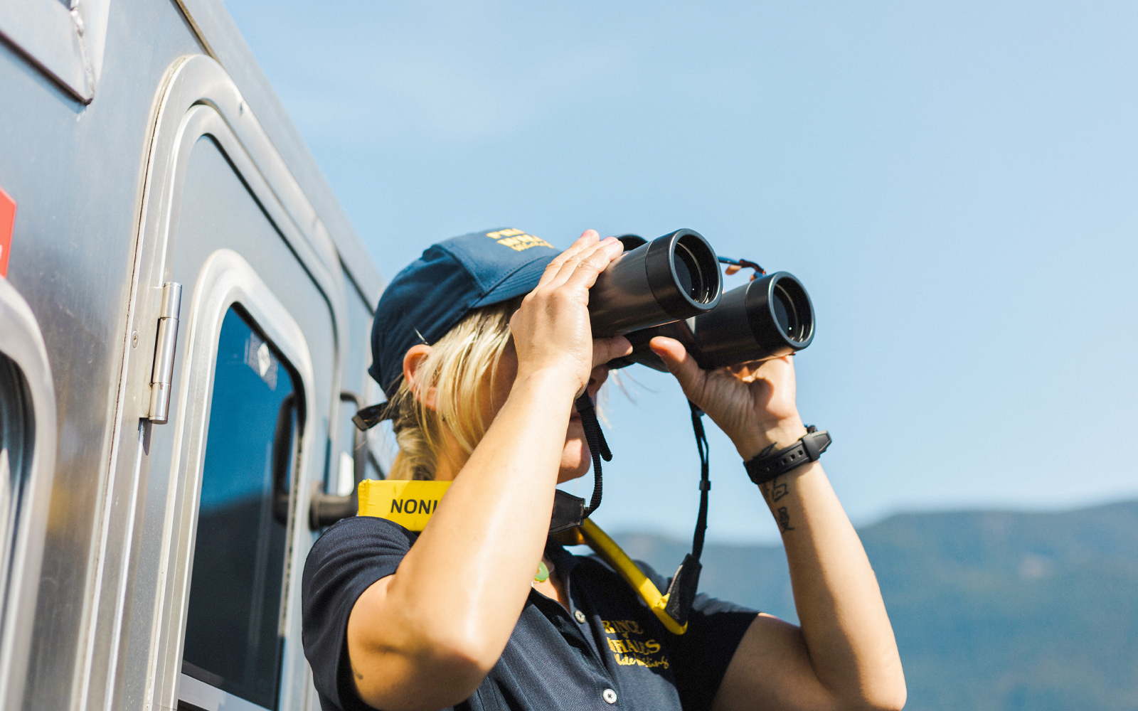 Woman using binoculars on a train, looking at distant mountains.