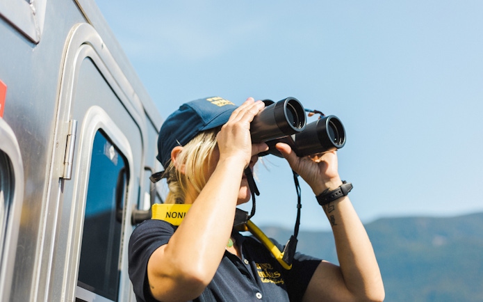 Woman using binoculars on a train, looking at distant mountains.
