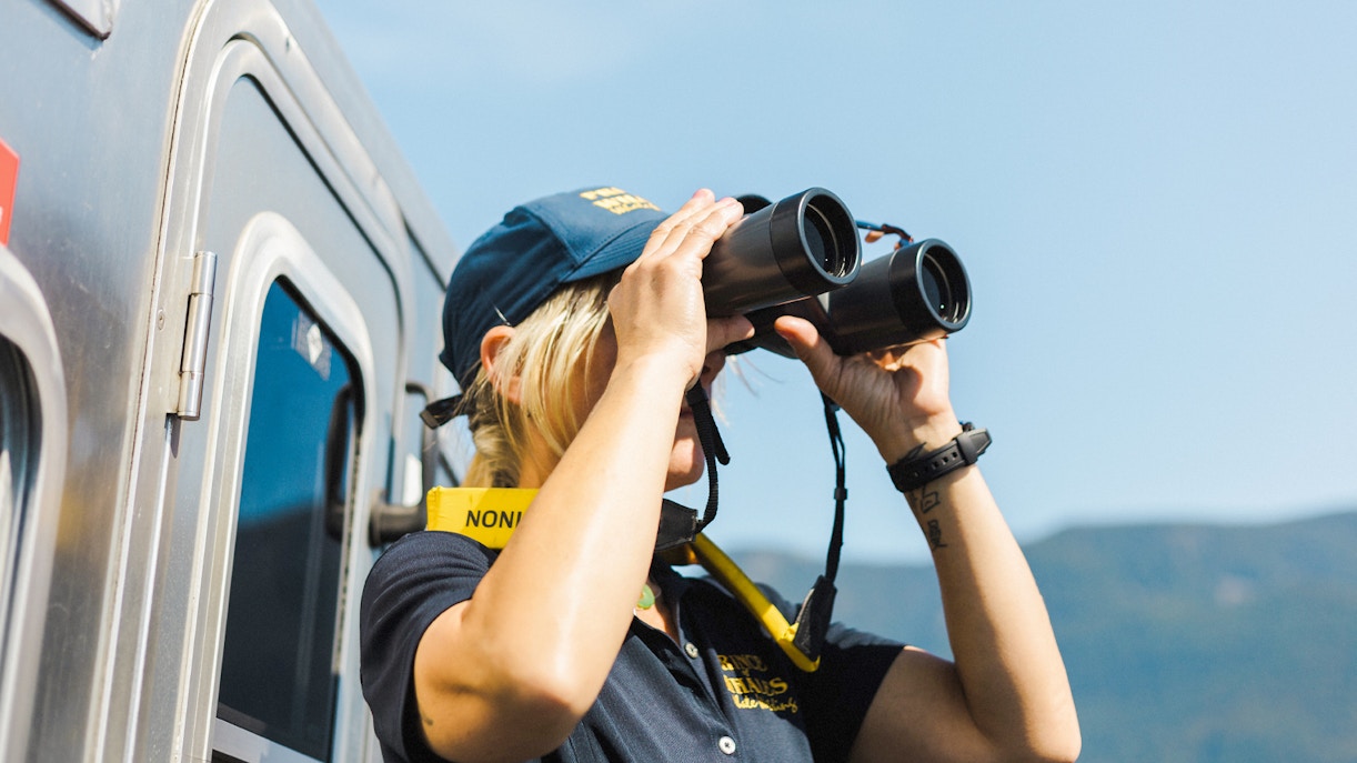 Woman using binoculars on Vancouver whale watching tour.