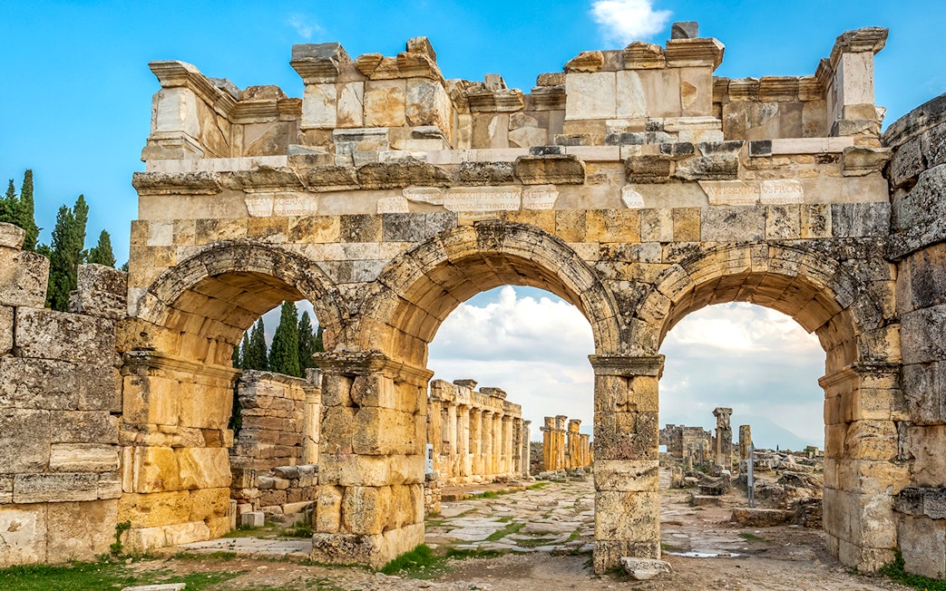 Facade of Domitian gates in ancient Hierapolis, Turkey, with stone arches and ruins.