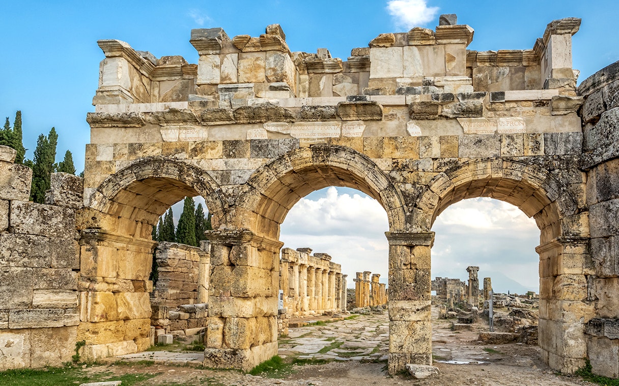 Facade of Domitian gates in ancient Hierapolis, Turkey, with stone arches and ruins.