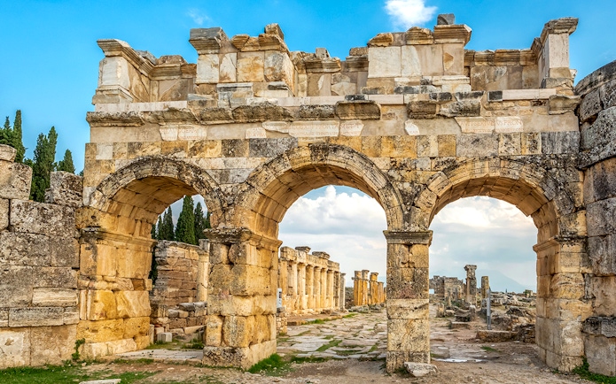 Facade of Domitian gates in ancient Hierapolis, Turkey, with stone arches and ruins.