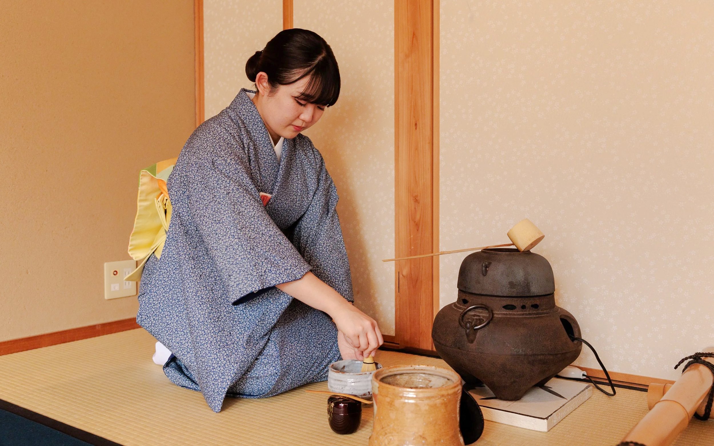 Tea ceremony participant preparing matcha in traditional Japanese room.