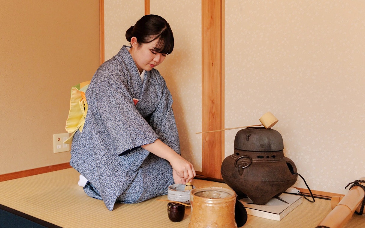 Tea ceremony participant preparing matcha in traditional Japanese room.