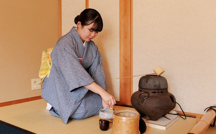 Tea ceremony participant preparing matcha in traditional Japanese room.