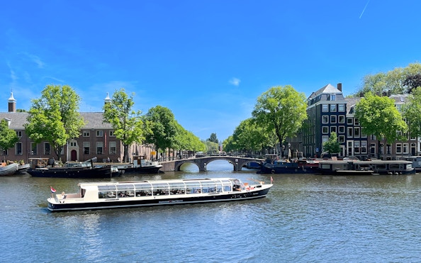 Canal cruise boat on Amsterdam's scenic canal with historic buildings and bridge.