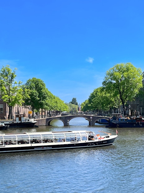 Canal cruise boat on Amsterdam's scenic canal with historic buildings and bridge.