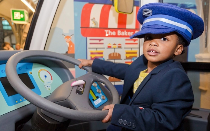 Child in a conductor's hat at London Transport Museum interactive exhibit.