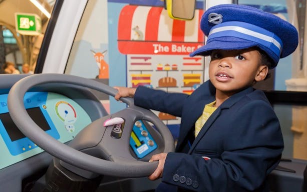 Child in a conductor's hat at London Transport Museum interactive exhibit.