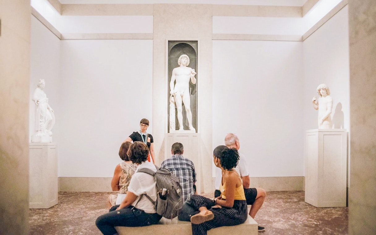 Guide and tourists viewing Greek and Roman statues at the Metropolitan Museum of Art.