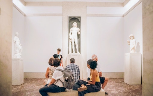 Guide and tourists viewing Greek and Roman statues at the Metropolitan Museum of Art.