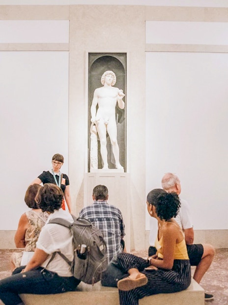 Guide and tourists viewing Greek and Roman statues at the Metropolitan Museum of Art.