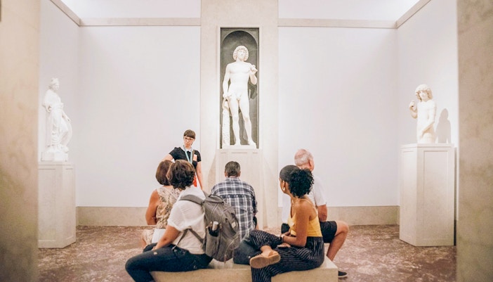 Guide and tourists viewing Greek and Roman statues at the Metropolitan Museum of Art, New York.